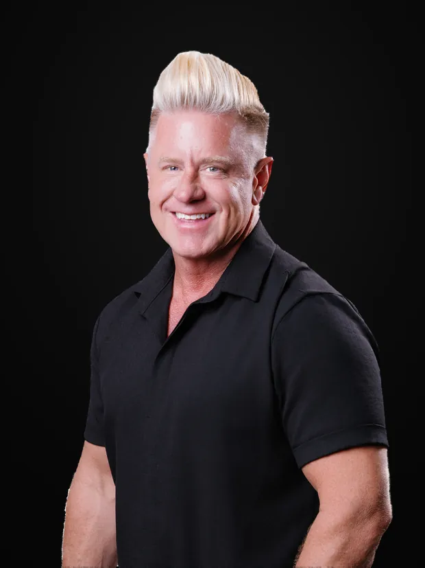 J Bravo smiling in a black shirt, one hand in his pocket